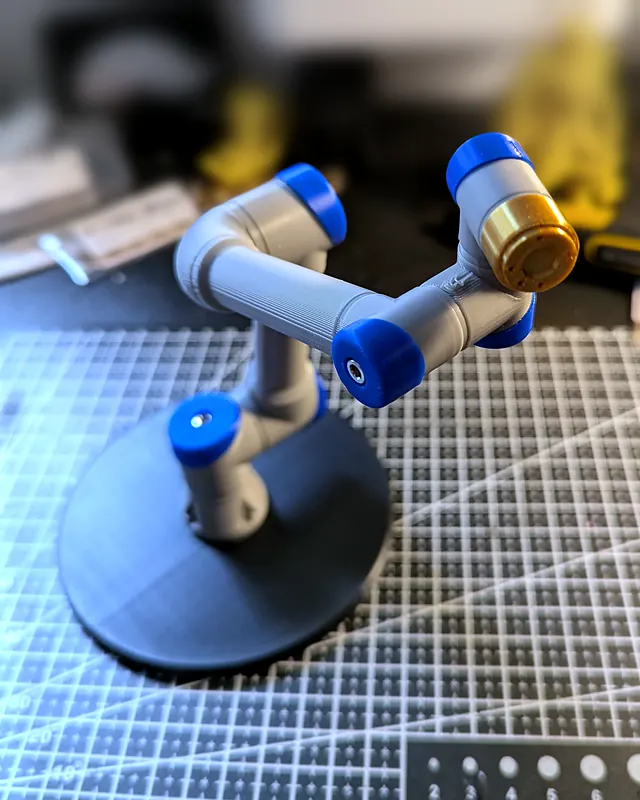 Brazo robot gris con tapas azules, estirado sobre su peana negra